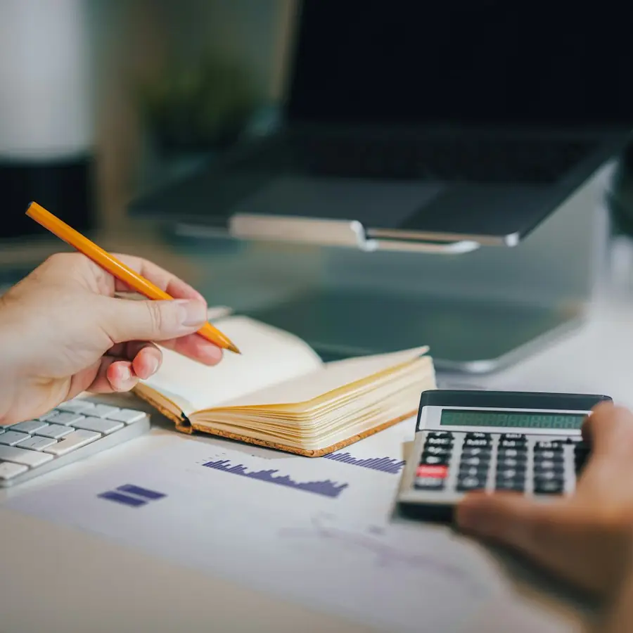 Iemand werkt de administratie bij met pen, notitieboek en rekenmachine.