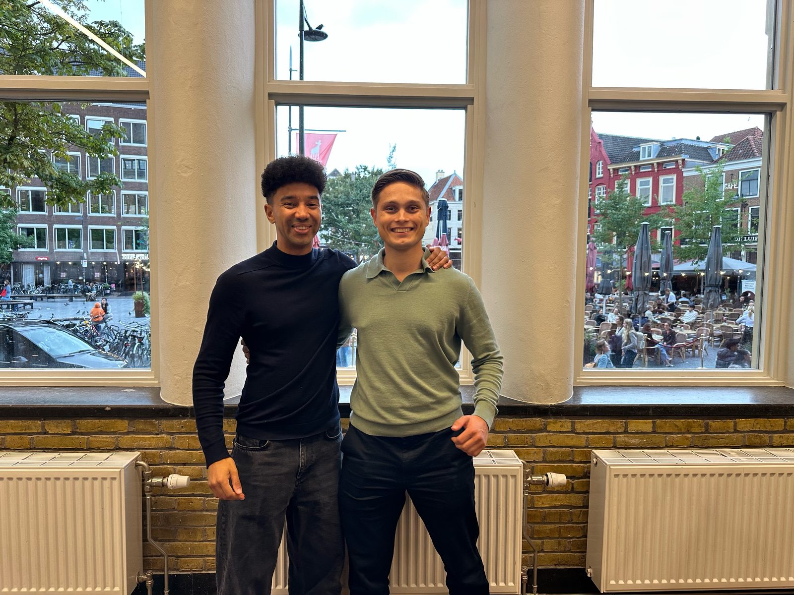 Camille en Jan lachend bij het raam, met Utrecht op de achtergrond.
